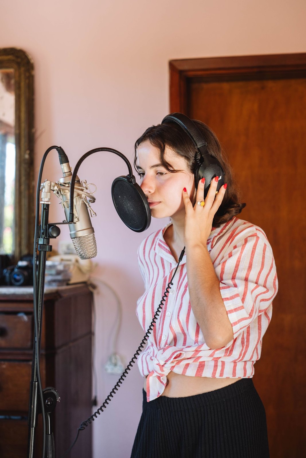 A performer at a studio microphone with headphones and pop filter.